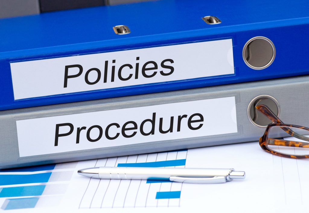 Humanising Policy and Procedures - Folders on a desk with a pen and glasses. Compliance